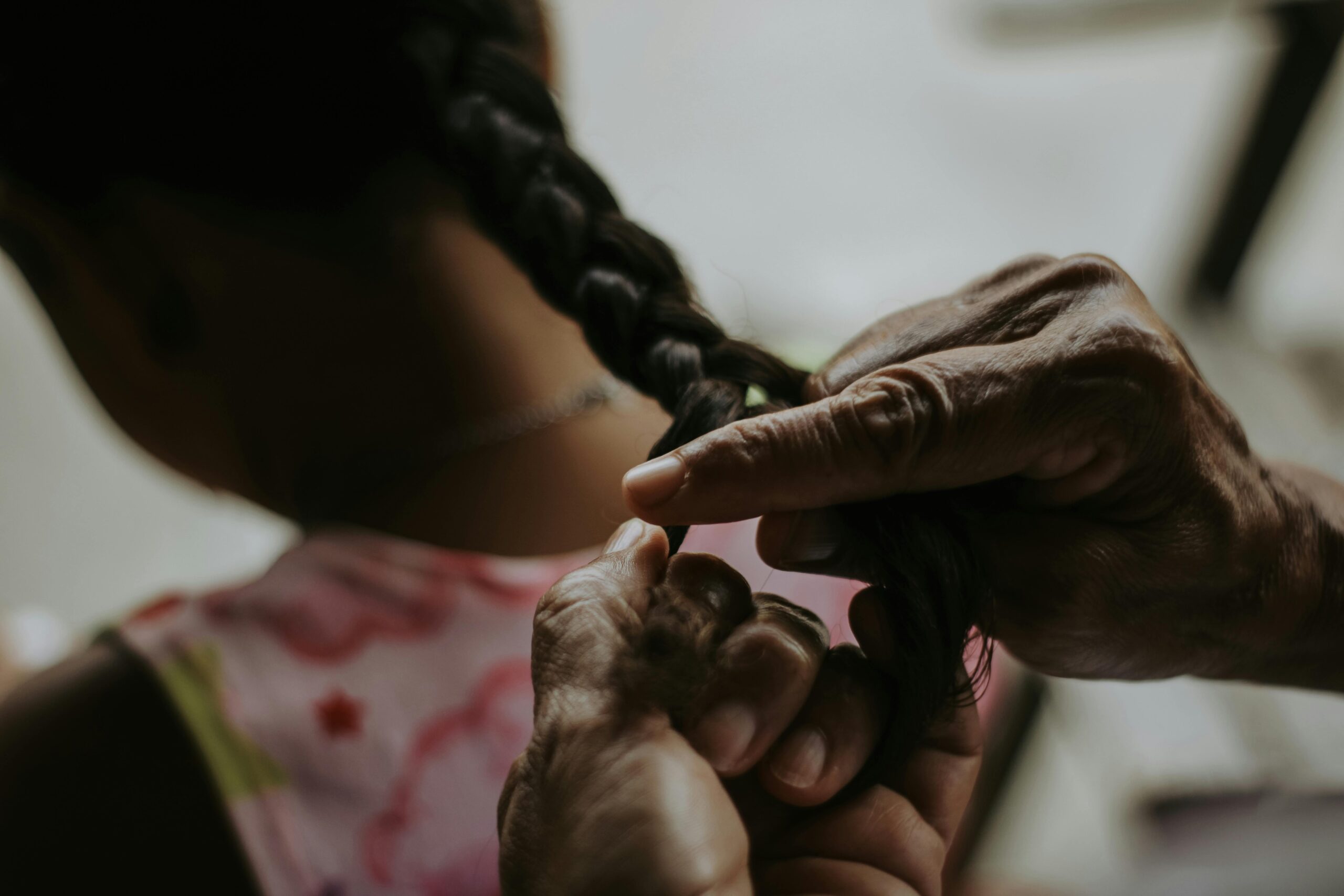 A close-up image capturing an adult braiding a child's hair indoors.