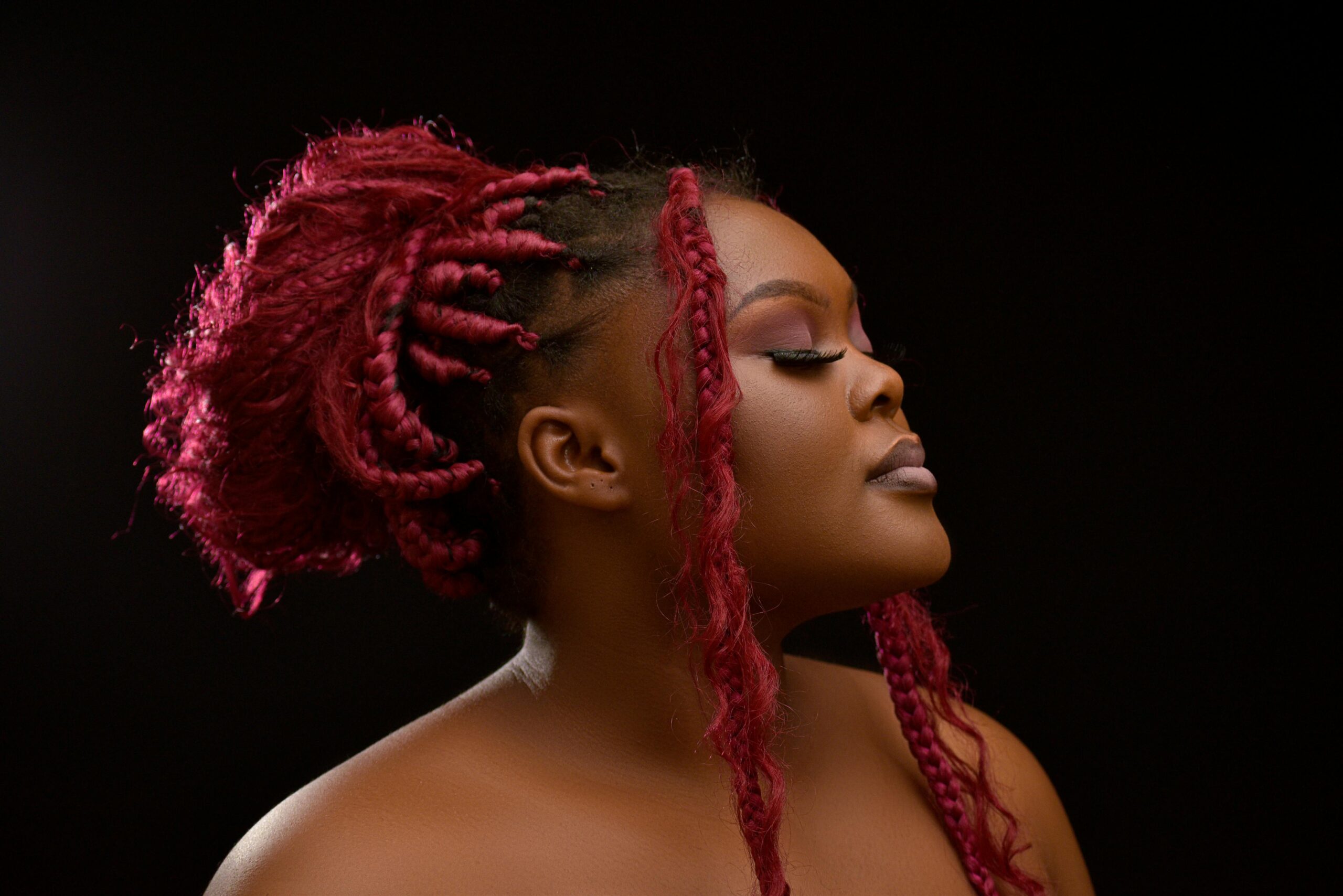 Artistic portrait of a woman with pink braided hair on a black background.